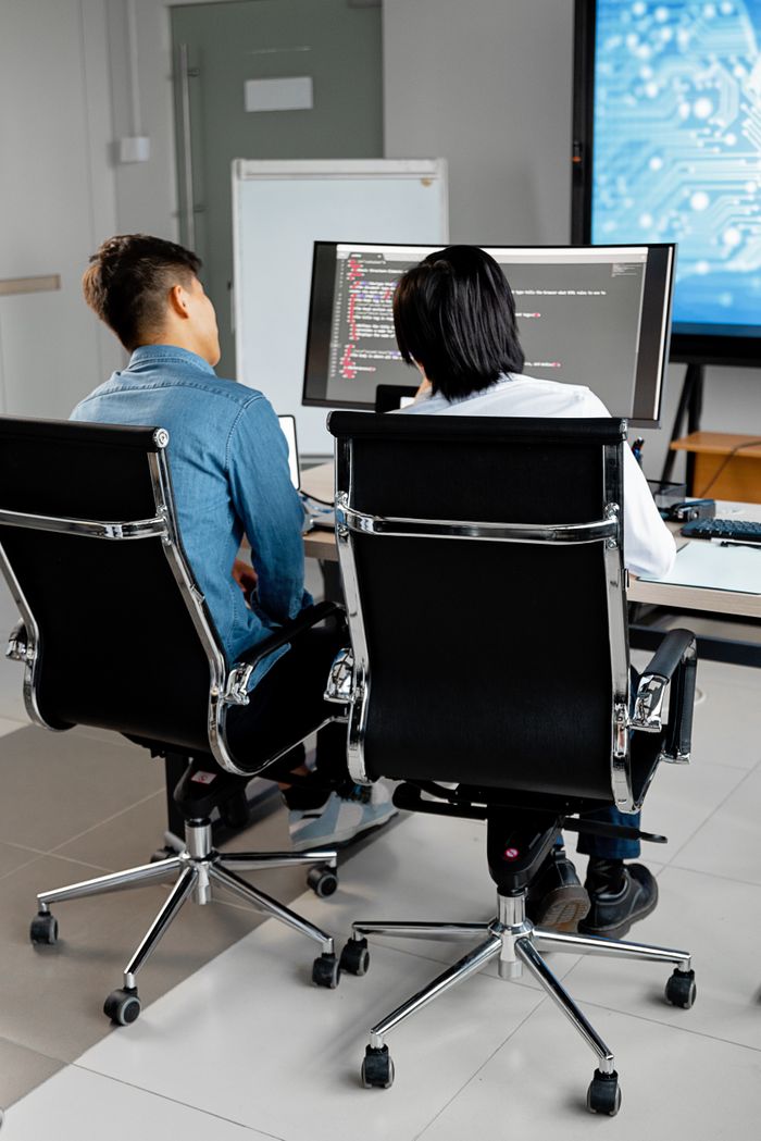 services-04 Two professionals collaborating at a desk with dual monitors in an office environment.
