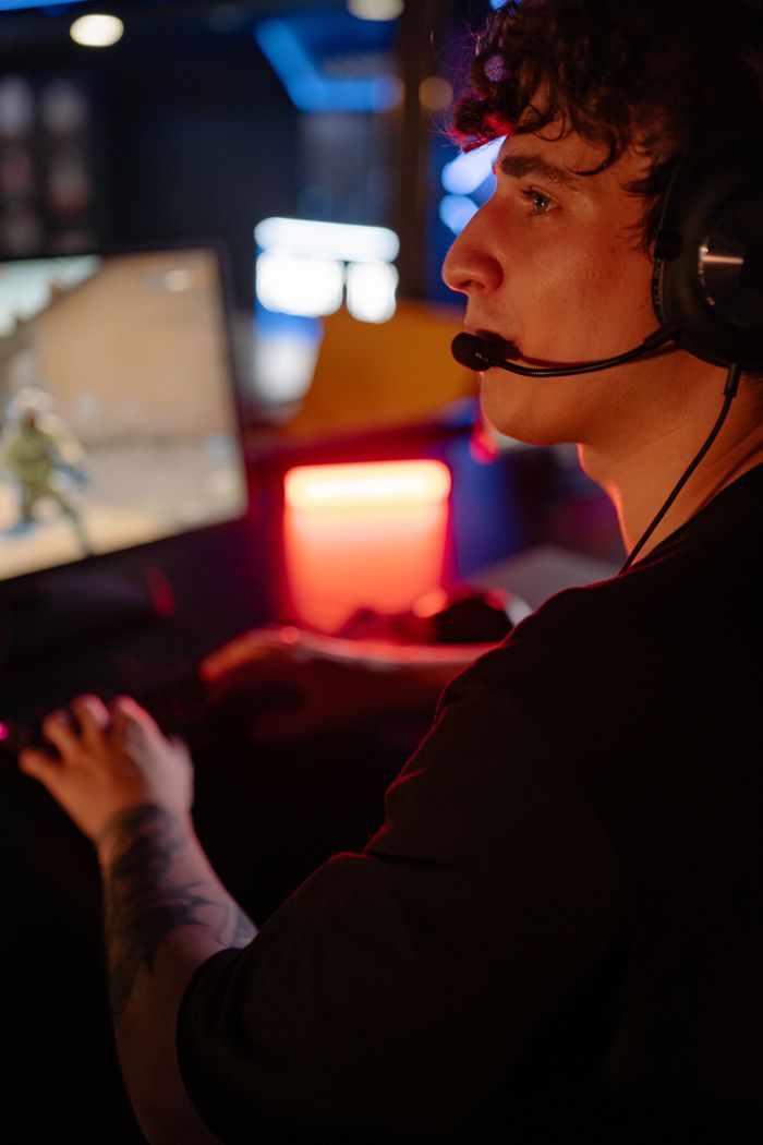 about-img A young man wearing a headset engrossed in an online gaming match with colorful lights.